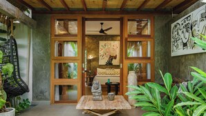 A room with a wooden ceiling, a ceiling fan, a table with a statue, a vase, and a painting on the wall. - Villa Gaya Ubud (Ubud)