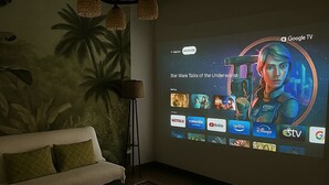 A living room with a large screen displaying a TV interface, a sofa, a coffee table, and a floor lamp.