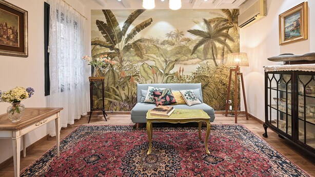 A room with a sofa, a patterned rug, a table with a book, a lamp, and a cabinet with glass doors.