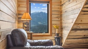 Ett mysigt rum med en soffa i läder, en lampa och en utsikt över bergen genom ett fönster.