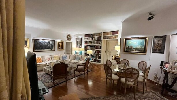 A spacious living room with a sofa set, dining table, and chairs. There are bookshelves and a television. - Charming bed & breakfast in enchanting Roma with AC and WiFi. (Roma)