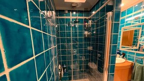 A bathroom with teal tiles, a glass-enclosed shower, and a sink with a mirror. - Charming bed & breakfast in enchanting Roma with AC and WiFi. (Roma)