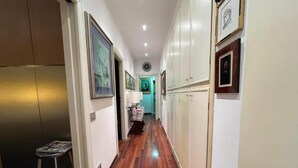 A narrow hallway with wooden flooring, white walls, and cabinets. There is a small stool with a magazine on it. - Charming bed & breakfast in enchanting Roma with AC and WiFi. (Roma)