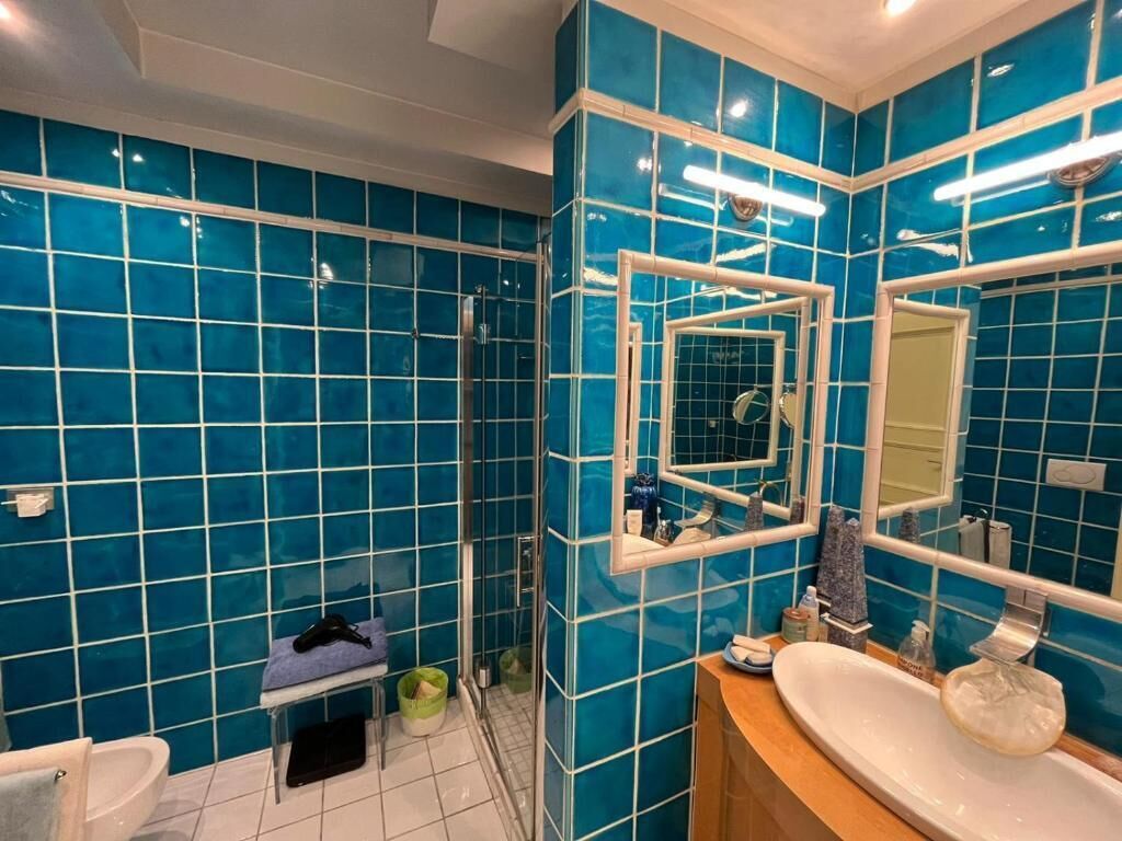 Ein Badezimmer mit blauen Fliesen, einem Waschbecken, einem Spiegel und einer Dusche.