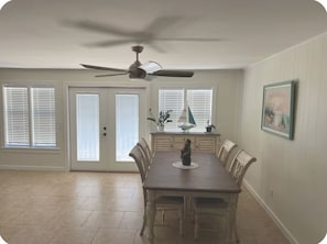 Comedor con mesa de madera, sillas, ventilador de techo y ventana con persianas.