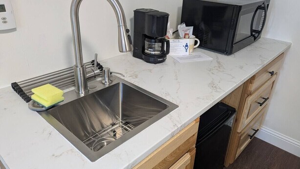 Een keuken met een roestvrijstalen spoelbak, een koffiezetapparaat, een magnetron en houten kastjes.