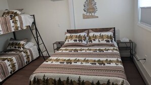 Een slaapkamer met een groot bed, een kleiner bed, een ladder, een nachtkastje en een luchtverkoeler aan de muur.
