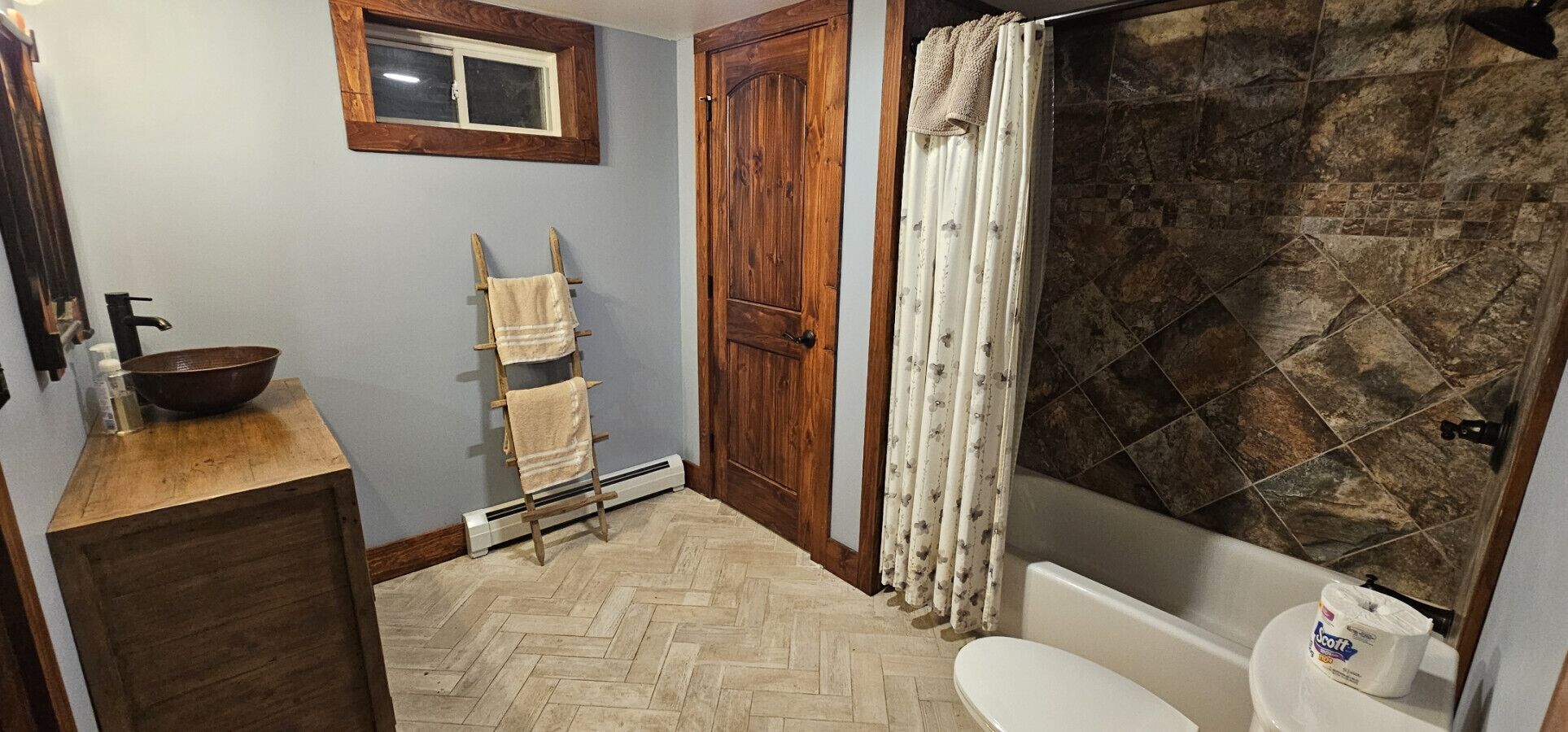 Une salle de bain avec un meuble-lavabo en bois, un évier, des toilettes et une douche avec un mur en pierre.