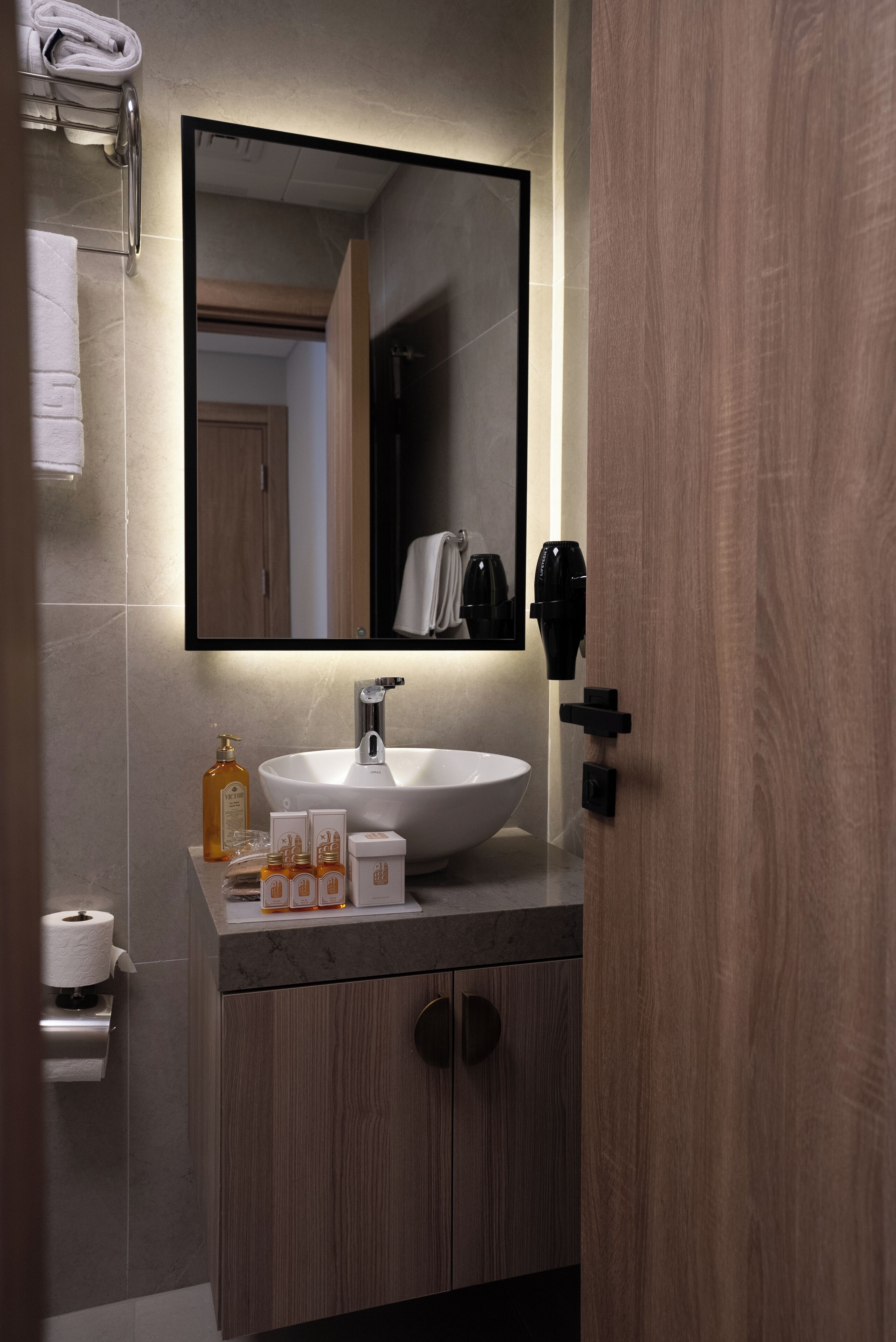 Une salle de bain moderne avec un grand miroir, un lavabo blanc et un meuble-lavabo en bois.