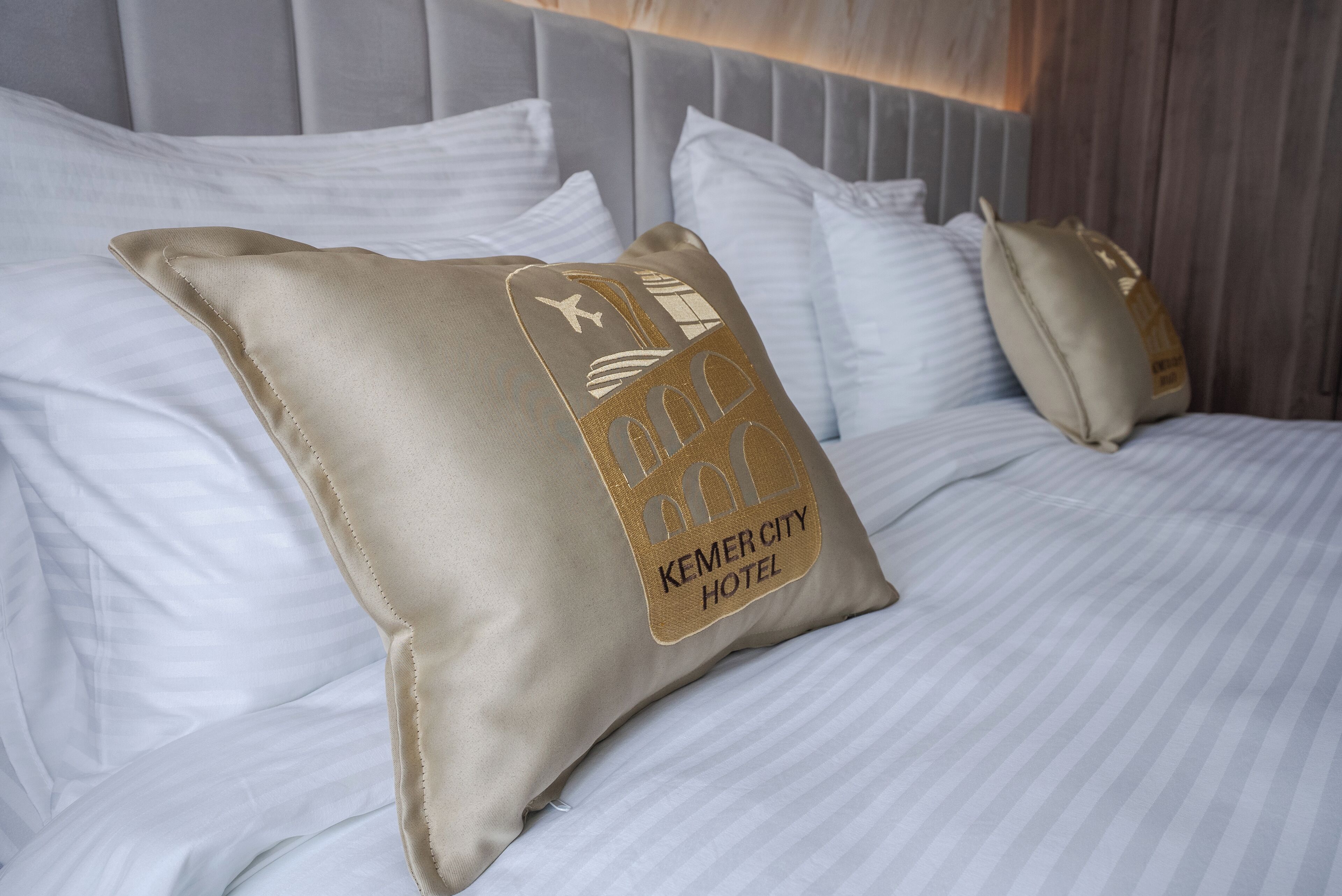 Una cama con sábanas blancas y un almohadón con el logotipo del Hotel Kemer City.