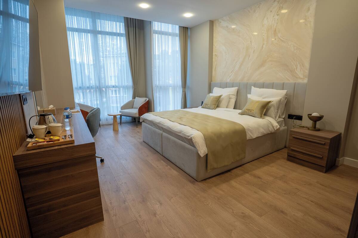 A modern hotel room with a large bed, a desk with a computer, a chair, and a small table.