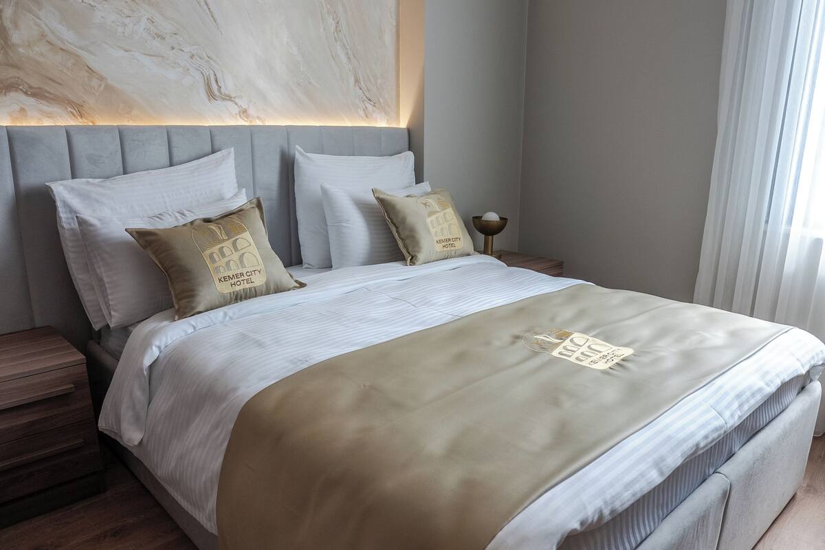A modern hotel room with a large bed, a headboard with a marble-like design, and a wooden floor.