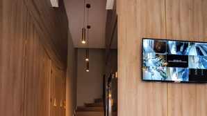Un interior moderno con paneles de madera, una escalera y un monitor de seguridad mostrando varias imágenes de cámaras.