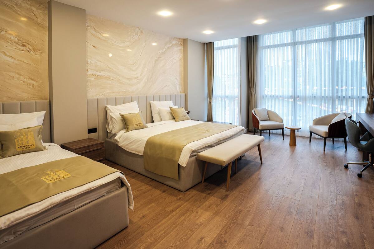 A hotel room with two beds, a bench, a desk, and a chair.