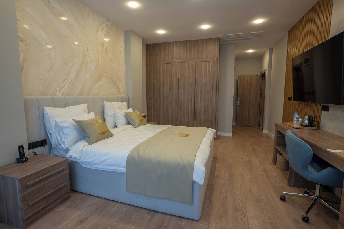 A modern hotel room with a large bed, a desk, and a TV.