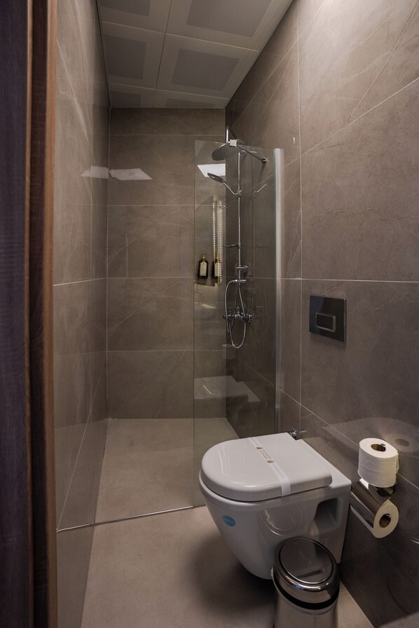 A modern bathroom with a glass-enclosed shower, a toilet, and a trash bin.