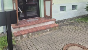 Une entrée d’immeuble avec une porte en bois, un petit porche et des marches menant à la porte.