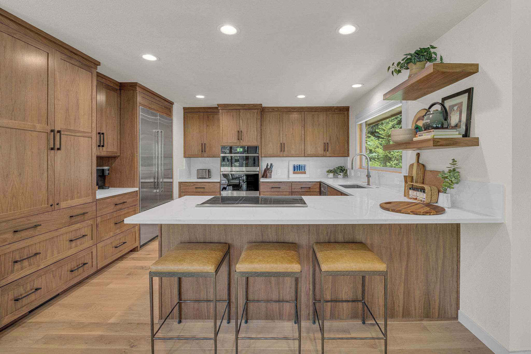 A modern kitchen with wooden cabinets, a central island with stools, and built-in appliances.