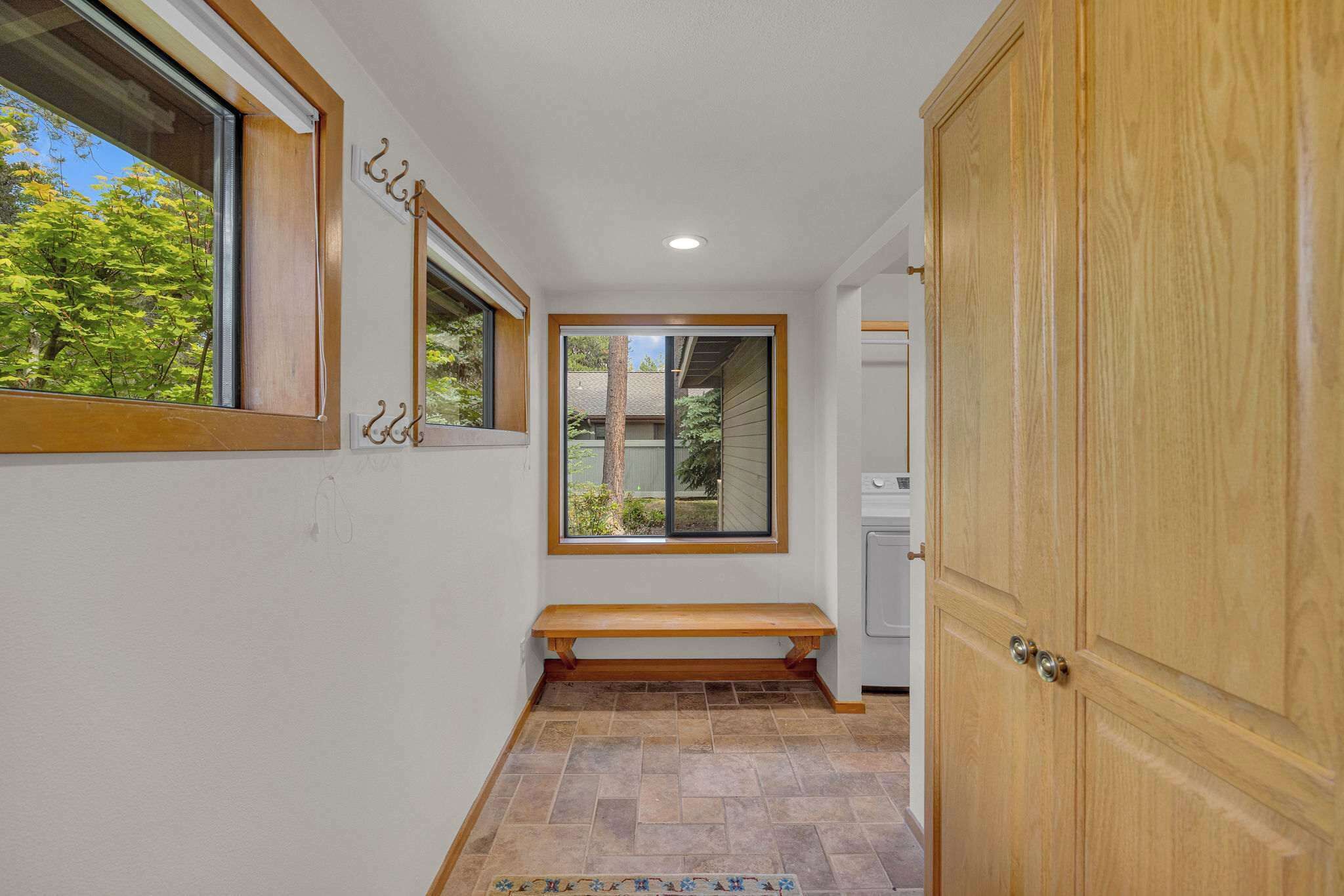 Un couloir avec un banc, une armoire en bois et une fenêtre donnant sur des arbres.