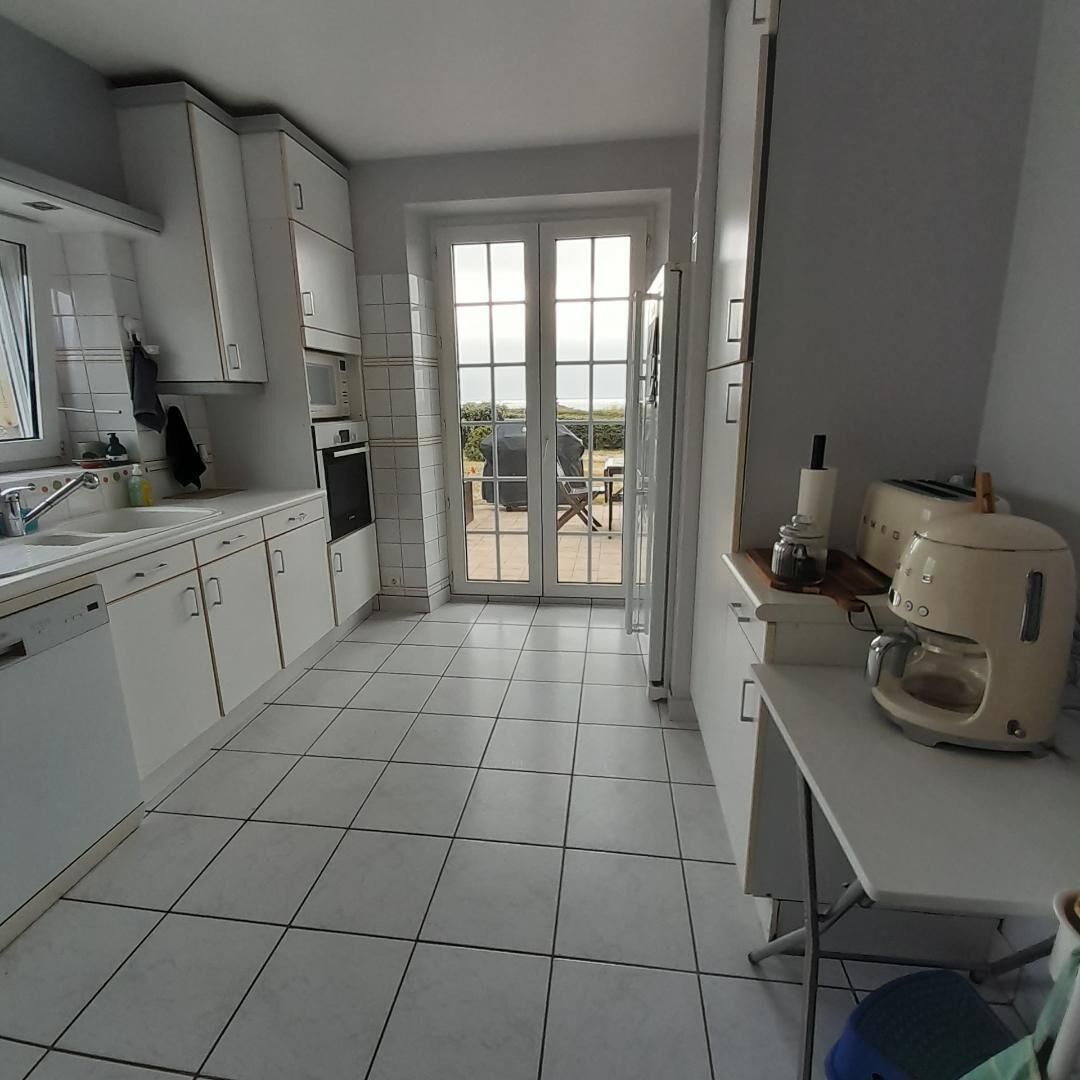 Eine moderne Küche mit weißen Schränken, einem Geschirrspüler, einer Kaffeemaschine und Blick durch Glastüren auf eine Terrasse.
