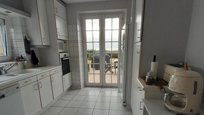 Una cocina moderna con armarios blancos, lavavajillas, cafetera y vistas a un patio exterior a través de puertas de vidrio.