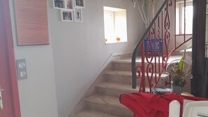 Una escalera con barandilla roja, un comedor con una silla blanca y una pared decorada con fotografías enmarcadas.