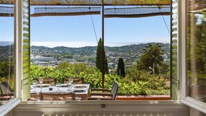 A dining area with a table set for two, overlooking a scenic view of a coastal town and hills. - Panoramic sea view villa & heated pool (Toulon)