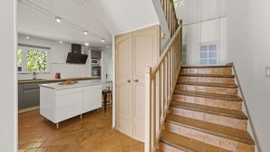 A modern kitchen with a central island, a dining area, and a staircase leading to another level. - Panoramic sea view villa & heated pool (Toulon)
