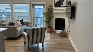 Un salon spacieux doté d’une cheminée, d’un téléviseur fixé au mur et d’une grande fenêtre donnant sur un balcon.
