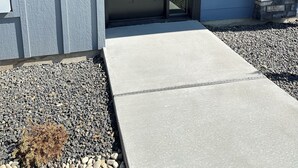 Une entrée moderne avec une porte sombre, un mur d’accent en pierre et un chemin en béton menant à l’entrée.