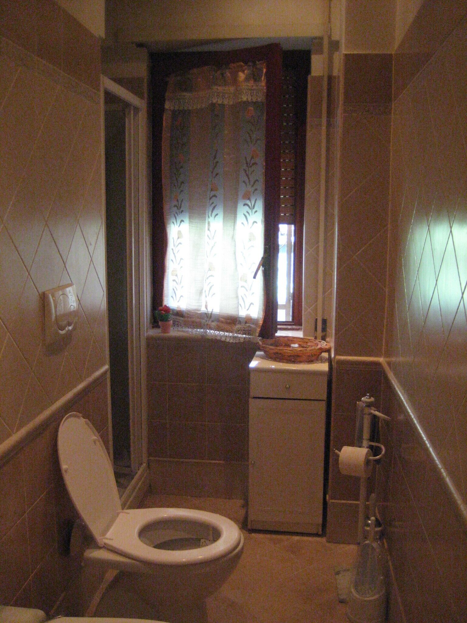 Un baño pequeño con inodoro, lavamanos y ventana con cortinas.