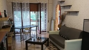 Una sala de estar con sofá, una mesa de centro, una mesa de comedor con sillas y una zona de cocina con mostrador y armarios.