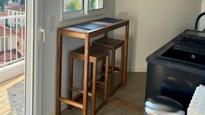 A small kitchen with a wooden table and stools, a black stove, and a view of the city through large windows. - SEASIDE Apartement, Calm, chill, Nice (Nice)