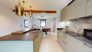A modern kitchen with a central island, pendant lights, a herringbone-patterned backsplash, and a view to the dining area.