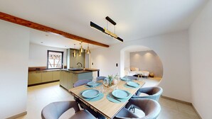 A modern kitchen with a wooden ceiling, a dining area with a wooden table set for four, and a living area with a sofa and a coffee table.