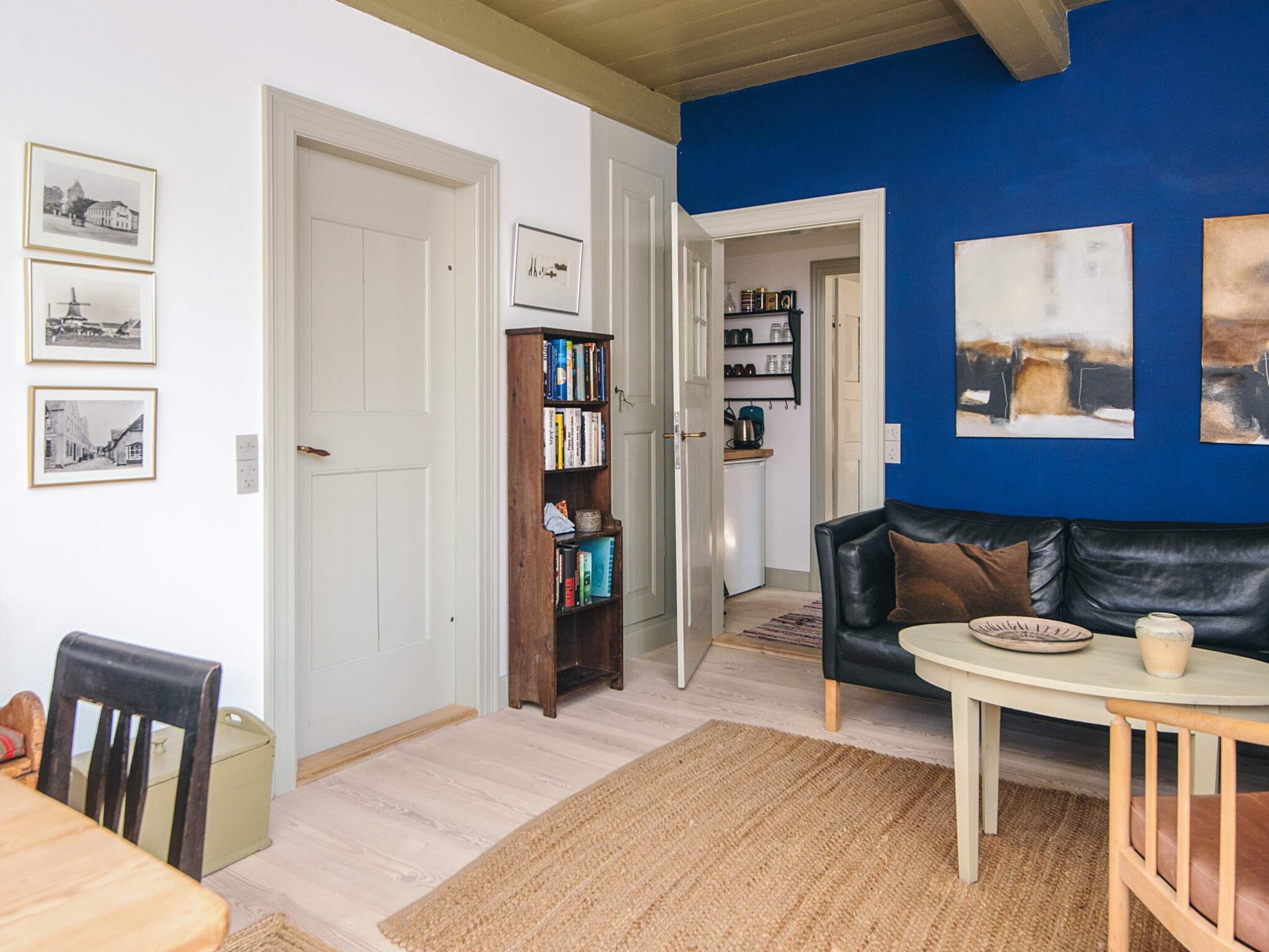 Una sala de estar con un sofá de cuero negro, una mesa de centro, una estantería y un comedor con mesa y sillas de madera.