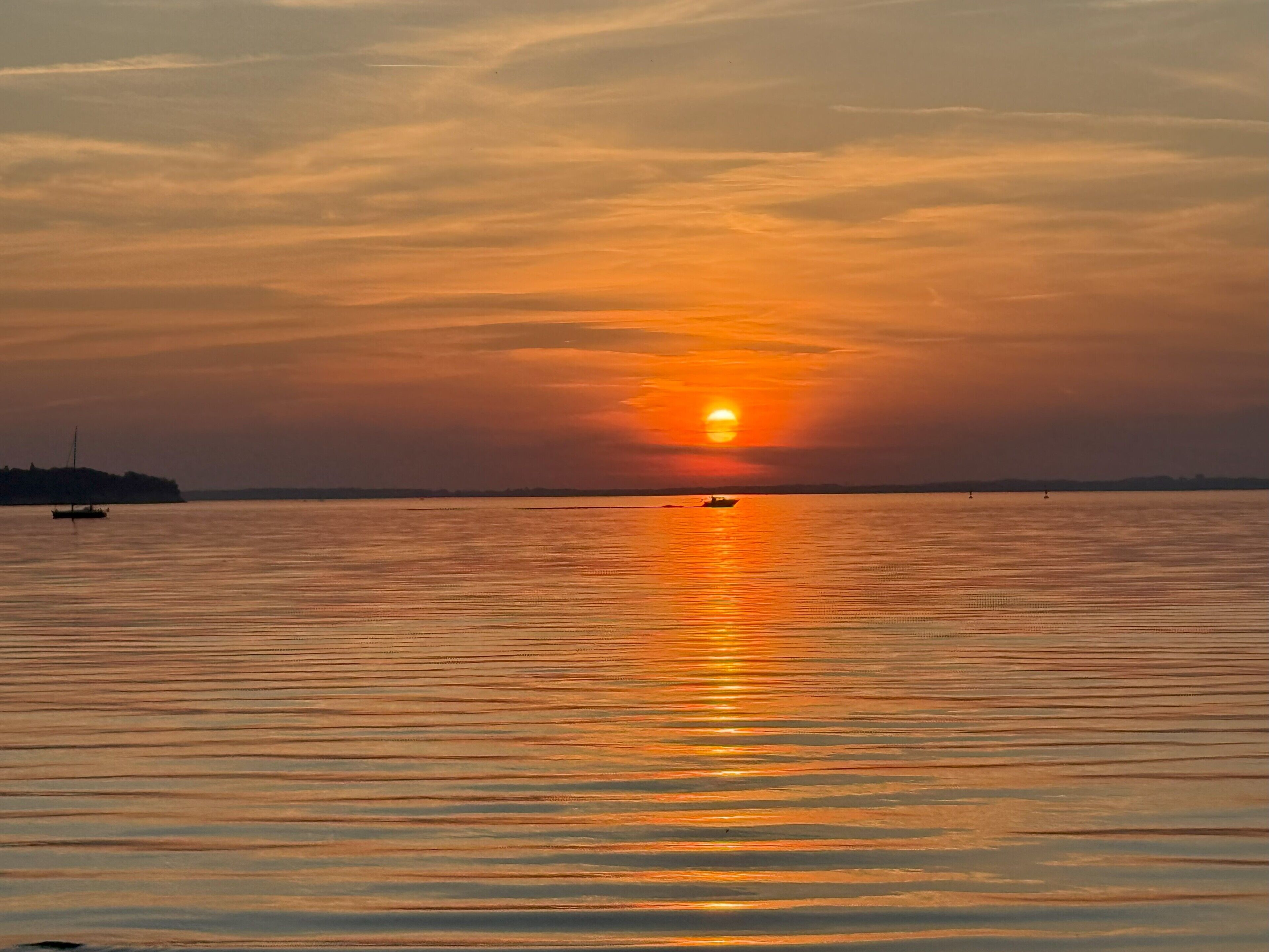 A sunset over a calm body of water with a distant shoreline and a small boat.