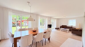 A spacious living room with a dining area, large windows, and a flat-screen TV. - Spacious, bright vacation home within walking distance of only 500m to the beach, with beautiful garden (Dassow)