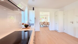 A modern kitchen with a large induction cooktop, a built-in oven, and a sink. There is a dining area with a table and chairs visible in the background. - Spacious, bright vacation home within walking distance of only 500m to the beach, with beautiful garden (Dassow)