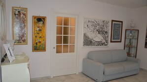 Ein Wohnzimmer mit einer Couch, einer Tür mit satinierten Glasscheiben und verschiedenen gerahmten Kunstwerken an den Wänden.