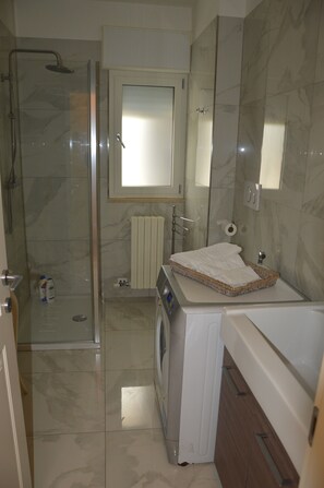 Un bagno con cabina doccia in vetro, lavatrice, lavabo con asciugamano e specchio.