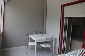 Un piccolo tavolo da pranzo bianco con quattro sedie in un angolo di una stanza con una parete grigia e una porta scorrevole in vetro.