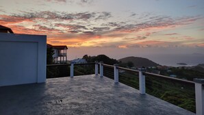 Un balcon offrant une vue sur un coucher de soleil se déclinant sur un paysage vallonné.
