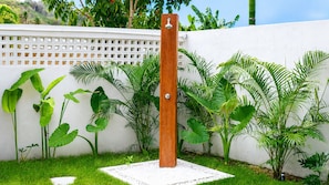 A wooden post with a showerhead, surrounded by lush green plants and a white wall. - Mediterrania Residences (Kuta)