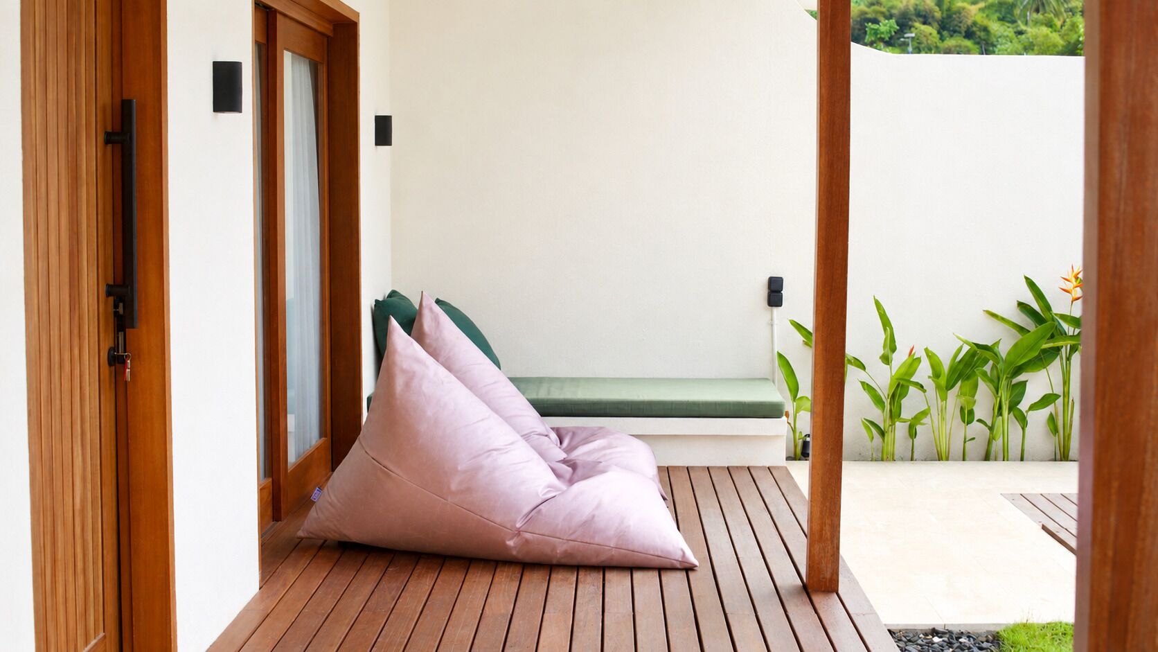 Una terraza de madera con un banco verde y dos pufs rosas.