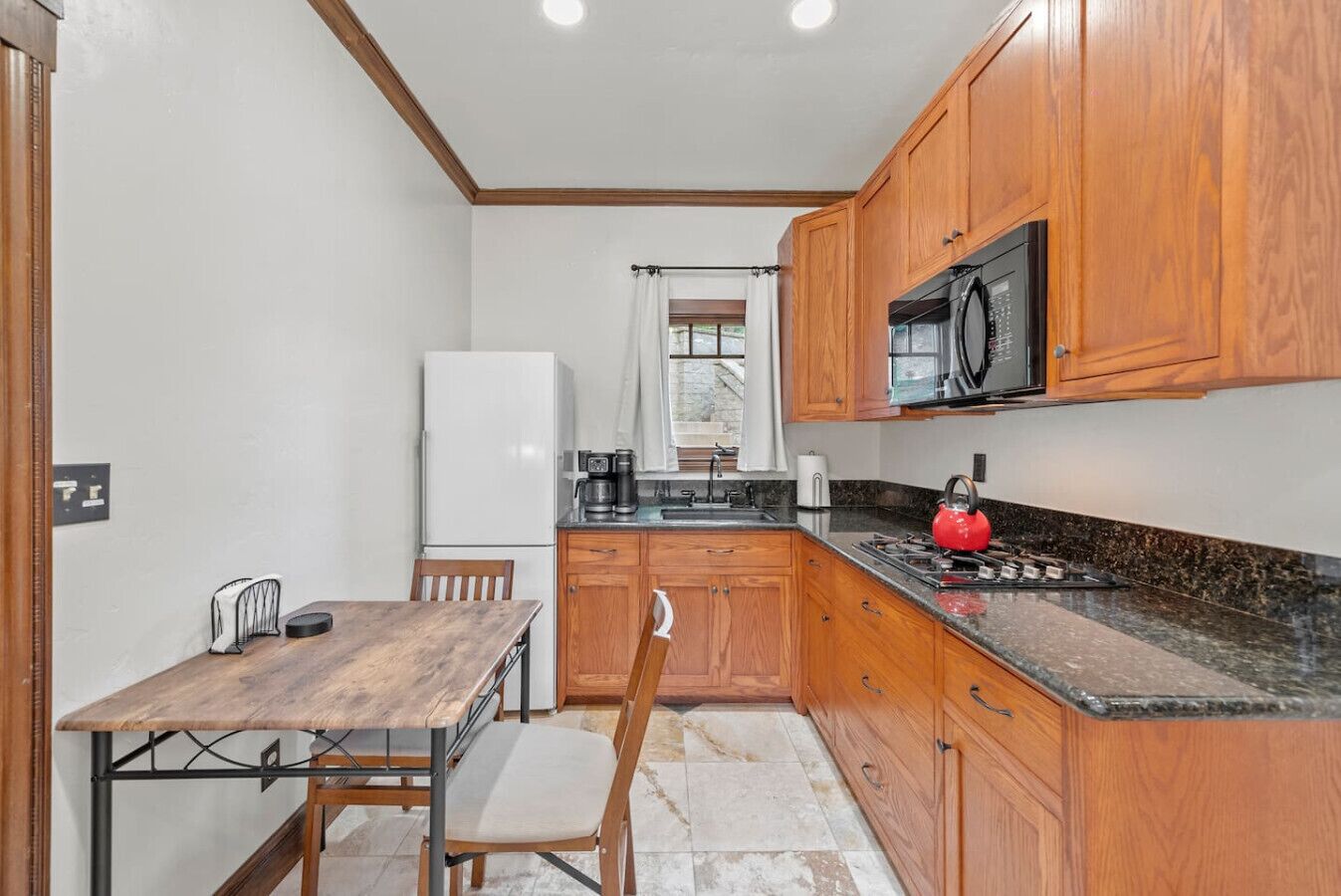 A compact kitchen with wooden cabinets, a stainless steel refrigerator, a microwave, and a red kettle on the countertop.
