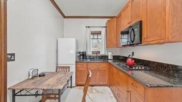 A compact kitchen with wooden cabinets, a stainless steel refrigerator, a microwave, and a red kettle on the countertop.