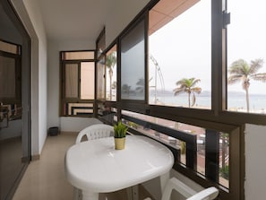 A balcony with a white table and chairs, a potted plant, and a view of the beach and palm trees. - Beachfront Home in Las Palmas Near Las Canteras (Las Palmas de Gran Canaria)