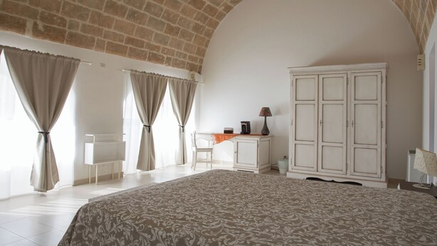 Un dormitorio con una cama grande, un escritorio, un armario y una ventana con cortinas.