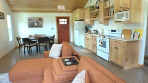 Amplia sala de estar con sofá modular, mesa de comedor con sillas y cocina con alacenas y electrodomésticos de madera.